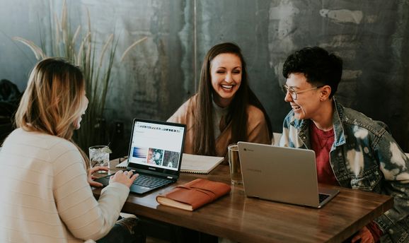 Three colleagues laughing together over their laptops